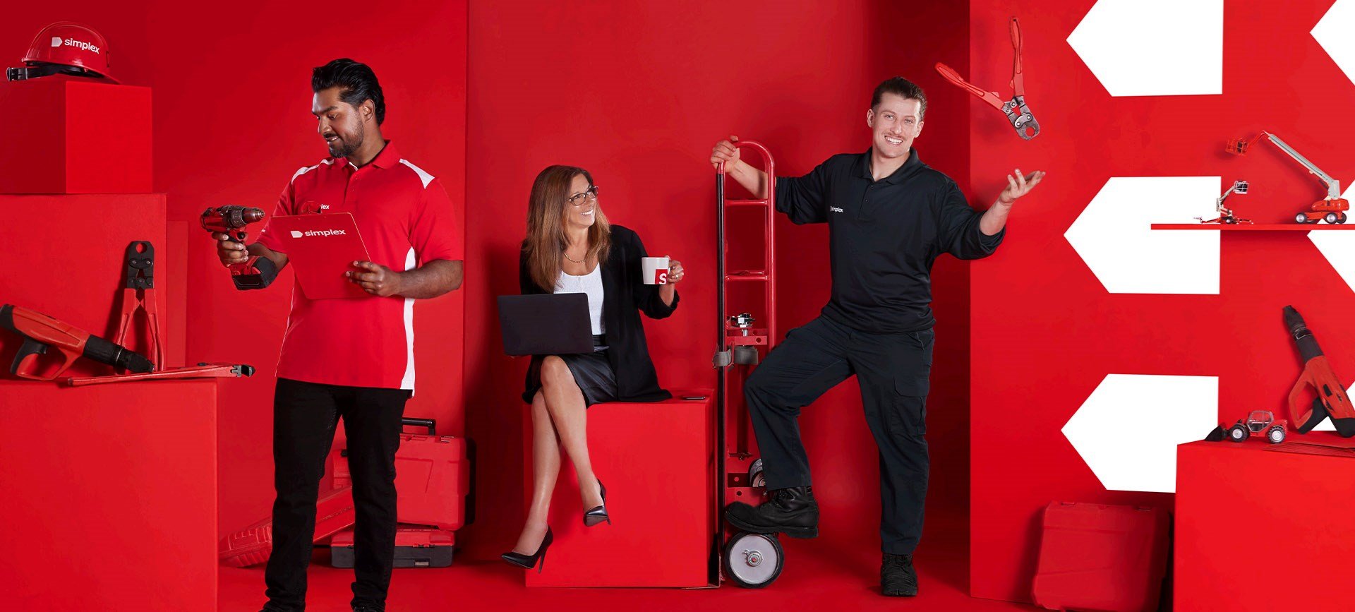 Photo d'un homme à gauche qui vérifie une perceuse, une femme au centre tient un ordinateur et une tasse, un homme à droite lance un outil.