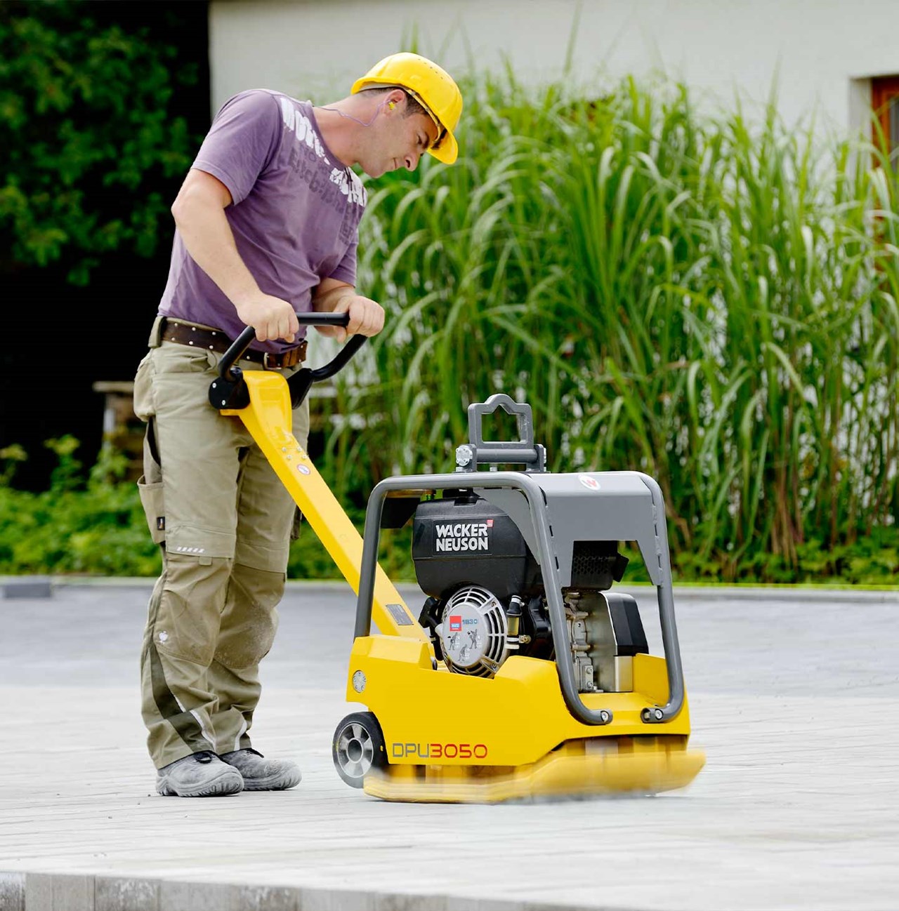 Opérateur utilisant une plaque vibrante Wacker Neuson jaune pour compacter les pavés-unis récemment posé.